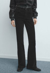 Czarne dzwony z podwyższonym stanem, gładką fakturą i klasycznym krojem z pięcioma kieszeniami, zestawione z dopasowaną kurtką i eleganckimi butami.