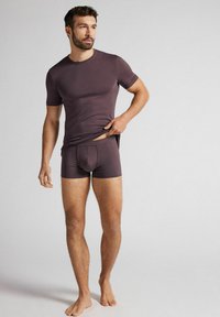 Mörkbrun t-shirt med slim fit och matchande boxershorts, båda tillverkade av ett mjukt material. Designen har en rund halsringning och korta ärmar.