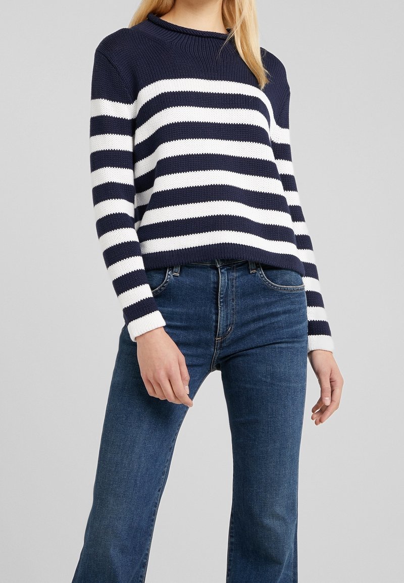 Gestreifter, navy- und weißer Strickpullover mit Rundhalsausschnitt, langen Ärmeln und gerippten Bündchen, getragen mit blauen Jeans.