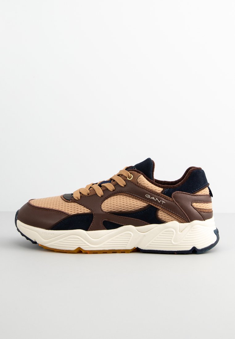 Light brown athletic sneaker with a mesh upper, dark blue accents, beige sole, and branded side detail. Rounded shape with textured panels.