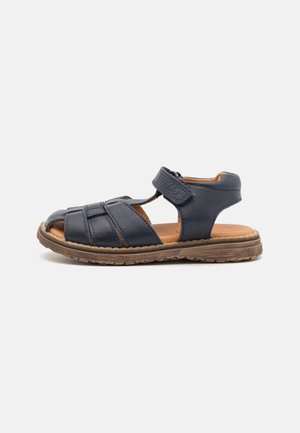 Gesloten sandalen van donkerblauw leer met verstelbare enkelband en gevoerde bruine zool, ontworpen voor comfort en duurzaamheid.