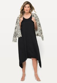 Schwarzes ärmelloses Kleid mit asymmetrischem Saum, kombiniert mit einem cremefarbenen Blazer mit schwarzem Leopardenmuster. Silbern ankle-strap Fersen.