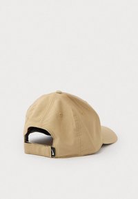 Gorra de béisbol ajustable beige con paneles cosidos, ojales de ventilación y una pequeña etiqueta de logo negro de Nike cerca de la correa trasera.