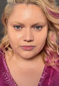 Nærbilde av en person med bølgete blondt hår med rosa høydepunkter, iført en teksturert, skinnende rosa topp med vertikale striper.