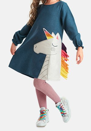 Blauwe spijkerjurk met een witte eenhoorn met een kleurrijke manen, gecombineerd met roze glitterlegging en zilveren sneakers met regenbooglacets.