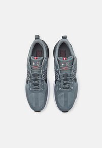 Szare buty sportowe z oddychającymi panelami siateczkowymi, okrągłymi sznurówkami, białą amortyzującą podeszwą oraz czerwonymi akcentami na języku i wkładce.