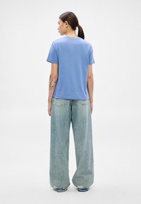 Svetlo modra bombažna majica z okroglim izrezom, kratkimi rokavi in sproščenim krojem, kombinirana z širokimi bledimi kavbojkami.