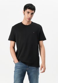 Black cotton t-shirt featuring a round neck, short sleeves, and a small logo accent. Paired with blue denim jeans.