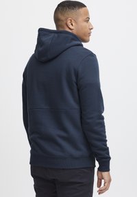 Hanorac cu glugă de culoare bleumarin, confecționat dintr-un amestec de bumbac, având un tiv și mansete ribbate, cu o textură netedă și un design minimalist.