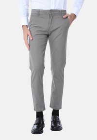Pantaloni in misto cotone grigi con vestibilità slim, chiusura a bottone e zip, tasche frontali e una superficie liscia. Indossati con mocassini neri.