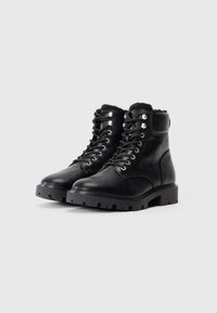 Botine negre din piele cu guler din blană sintetică, vârf rotund și talpă din cauciuc rezistent. Prezintă ochiuri argintii și șireturi negre.