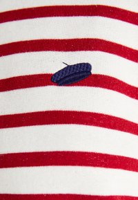 Tissu rayé rouge et blanc avec un détail brodé bleu marine ressemblant à un béret. Texture lisse, avec des rayures étroites et régulières.