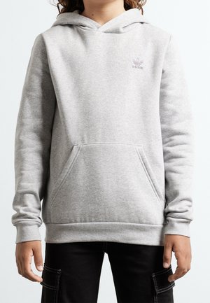 Enfant portant un sweat à capuche Adidas gris clair avec une poche kangourou à l'avant et un pantalon cargo noir sur un fond uni.