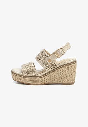 Sandalia cuña con correas sintéticas doradas perforadas, hebilla ajustable y suela envolvente de yute. Plantilla suave de color claro.