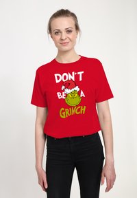 Červené bavlněné tričko s potiskem zeleného Grinche v Santově klobouku a textem "NEBUĎ GRINCH" v tučných bílých a zelených písmenech.