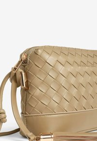 Borsa a tracolla in pelle intrecciata beige con superficie testurizzata, hardware dorato, chiusura a zip e dettaglio in frange decorativo.