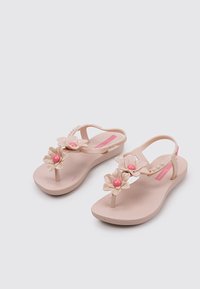Chanclas de plástico en tonos rosa y beige con un diseño floral que presenta dos flores y cuentas rosa en las correas. Suela plana con superficie texturizada.