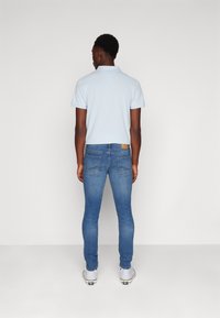 Ljusblå polo t-shirt kombinerad med figurnära blå jeans. Skorna är vita med svarta detaljer. Detaljer inkluderar en design på bakfickan och ett märke.