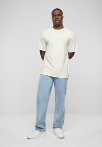 Lys beige bomull t-skjorte med korte ermer og rund hals, sammen med lyseblå dongeribukser og hvite joggesko.
