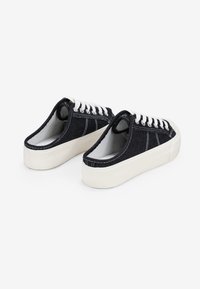 Zapatos slip-on de mezclilla negra con cordones blancos y una suela de goma blanca, que cuentan con detalles de costura y un diseño de punta redondeada.