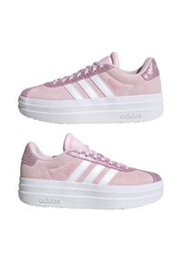 Zapatillas de ante rosa con un diseño de tres franjas blancas, acentos rosados texturizados y una suela plataforma blanca gruesa. Marca en el talón y en el lateral.