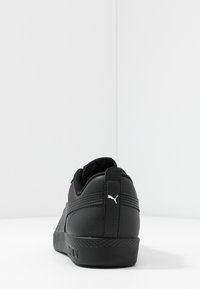 Zapatilla negra con parte superior de cuero sintético liso, acentos texturizados, cuello acolchado y logo blanco en el talón. Diseño de corte bajo con suela de goma.