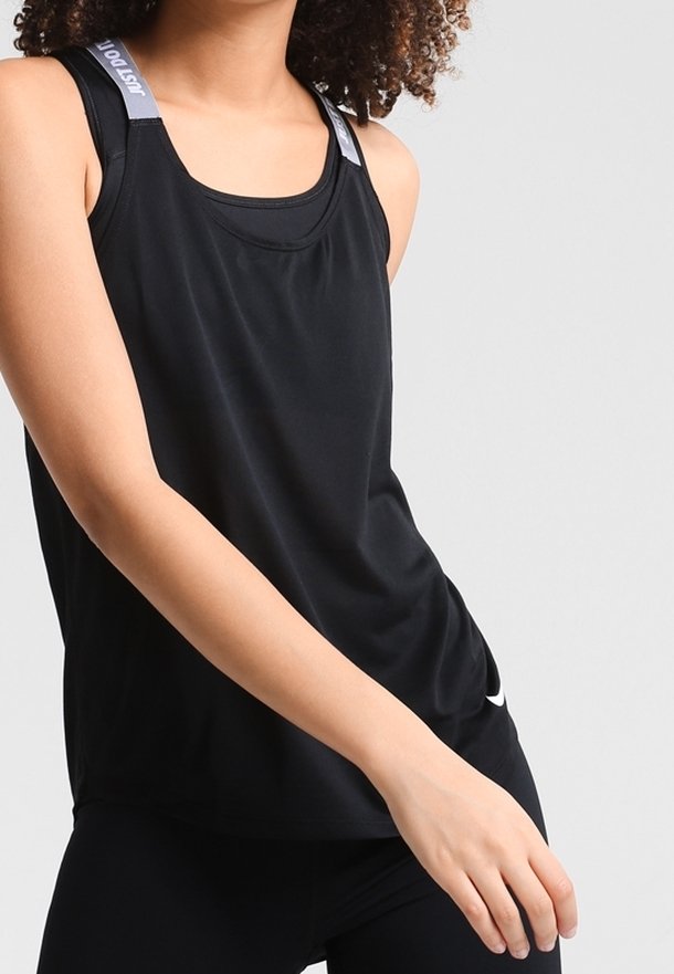 Personne portant un haut de sport noir sans manches avec des bretelles grises aux épaules portant l’inscription « JUST DO IT », debout devant un fond clair uni.
