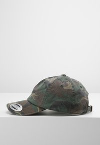 Căciulă de camuflaj în nuanțe de verde și maro; fabricată din material textil; cu margine curbată; curea ajustabilă la spate; prezintă orificii de ventilație.