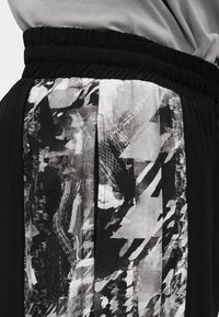 Μαύρη ελαστική μέση σε παντελόνι με κάθετο αφηρημένο ασπρόμαυρο σχέδιο στο πλάι.