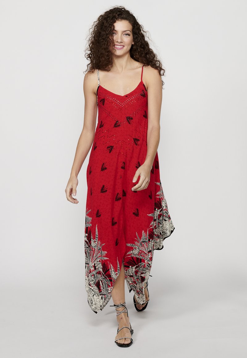 Robe maxi sans manches rouge avec décolleté en V, ornée de motifs de feuilles noires et d'accents argentés, présentant un ourlet asymétrique et une texture douce.