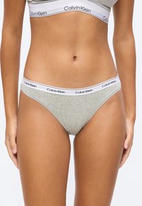 Žena v sivej spodnej bielizni Calvin Klein so sivými elastickými pásmi s logom Calvin Klein na pásoch.