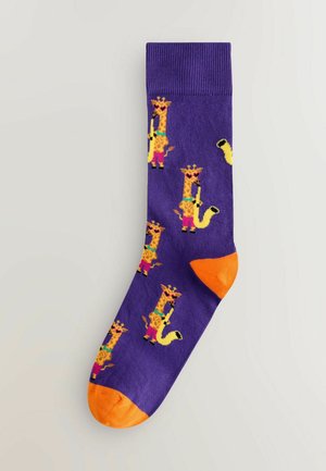 Lila strumpor med ett lekfullt giraffmönster i ljusa gula och rosa accenter. Tå- och hälområdena är orange.