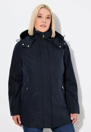 Giacca impermeabile blu con zip frontale, cappuccio regolabile e tasche laterali con zip. Presenta una trama morbida e un design aderente.