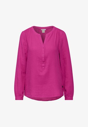 Fuksia pitkähihaisessa paidassa on kevyttä kangasta, pyöreä kaula-aukko ja nappiluukku, jossa on hieman kaareva helma. Vetskattuja hartioita.