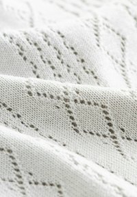 Tejido de punto gris claro con un patrón de diamante texturizado, que presenta puntos de tejido abiertos y un aspecto suave y transpirable.