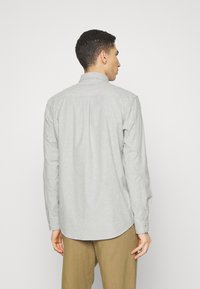 Camisa de botones de manga larga en gris claro con cuello, yugo trasero recto y puños abotonados; presenta una tela suave y texturada.