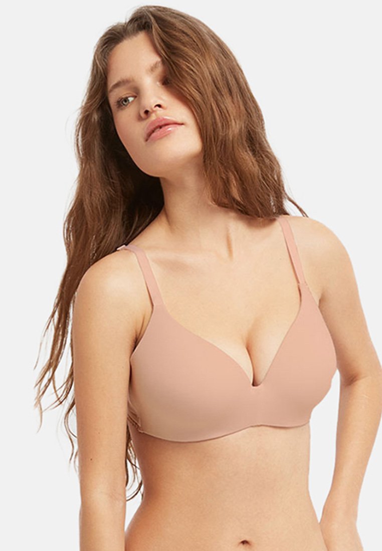Soutien-gorge léger beige avec un col en V, des bretelles ajustables et un design sans coutures. Fabriqué en matériau lisse et extensible pour le confort.