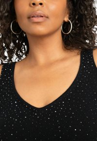 Svart ärmlös topp med V-ringning och en strukturerad stickad design, dekorerad med spridda metalliska paljetter för extra detalj.