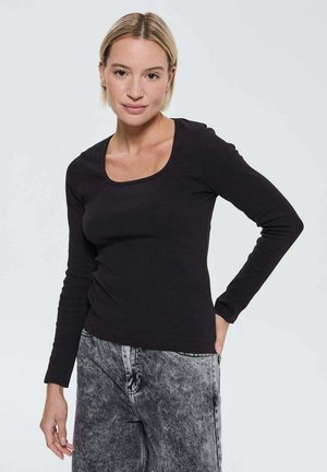 Haut noir à manches longues avec un décolleté arrondi, texture côtelée et design ajusté, associé à un pantalon en denim gris taille haute.