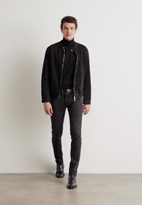 Black zippered jacket over a black turtleneck, paired with dark jeans and black ankle boots. Minimalist design against a light background.