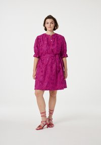 Fuchsia jurk met bloemenborduursel, korte puffmouwen, knoopsluiting aan de voorkant en bijpassende riem. Gecombineerd met roze sandalen met bandjes.