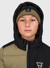 Fiatalember két színű, fekete és olíva télikabátban, kapucnival és olívazöld kötött sapkával, amelyen a "Brunotti" felirat található.