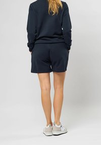 Ensemble en sweat-shirt bleu marine et short, en tissu doux, coupe décontractée, col rond classique, et teinte assortie. Des baskets blanches complètent le look.