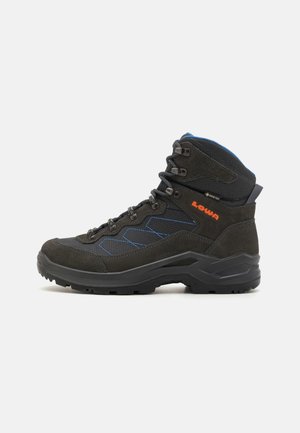 Botte de randonnée mi-haute noire et bleue avec semelle robuste, œillets métalliques, logo orange "Lowa" et étiquette Gore-Tex sur le côté.