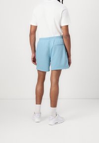 Ljusblå bomullsshorts med elastisk midja, sidfickor, en bakficka och en avslappnad passform. Bärs med en vit T-shirt och sneakers.