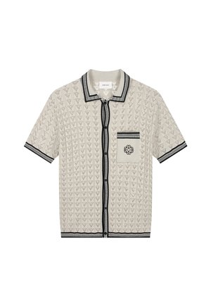 Short-sleeve beige knit shirt with black trim, button front, patterned texture, and a pocket featuring a black embroidered emblem.