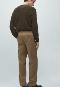 Brązowy sweter o fakturowanej powierzchni, z luźnym krojem. Beżowe spodnie z elastycznym pasem i tylnymi kieszeniami. Ciemne buty dopełniają strój.