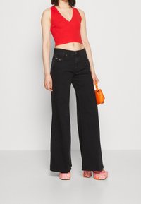 Top court rouge, jeans noirs évasés et chaussures à plateforme imprimées de flammes roses. Petit sac à main orange en accessoire.