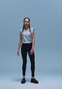 Hall hõlmikuta ülemine osa lõdva lõikega, kombineeritud mustade kitsaste teksapükste ja mustade platvormkingadega. Lihtne disain ja ühevärvilised toonid.