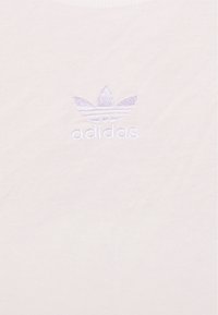 Ljusfärgad bomullströja med en liten lavendelfärgad broderad adidas-logga centrerad på bröstet. Mjuk och slät textur.